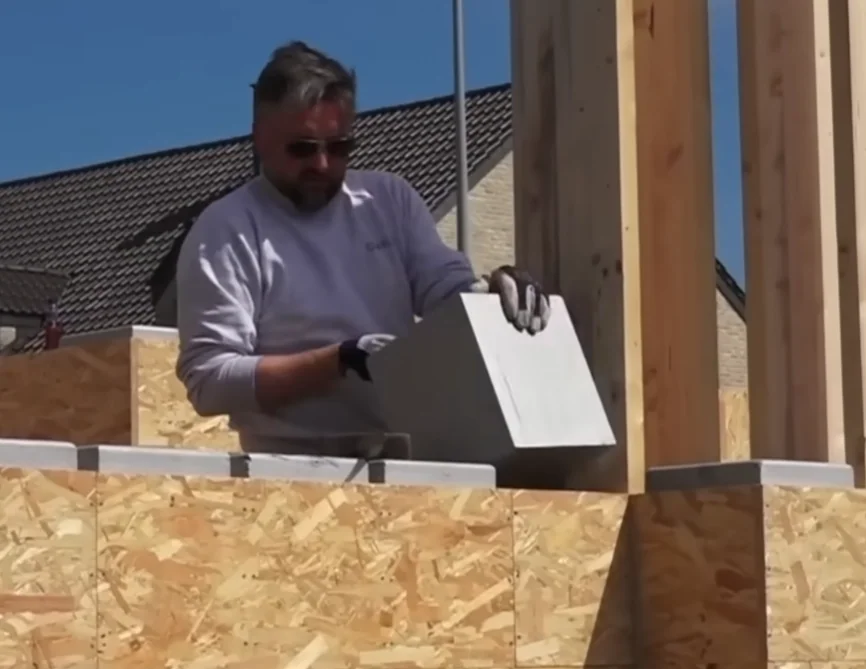Um construtor encaixando um bloco isolante branco de EPS dentro da estrutura de madeira OSB no andar superior de uma casa Gablok.
